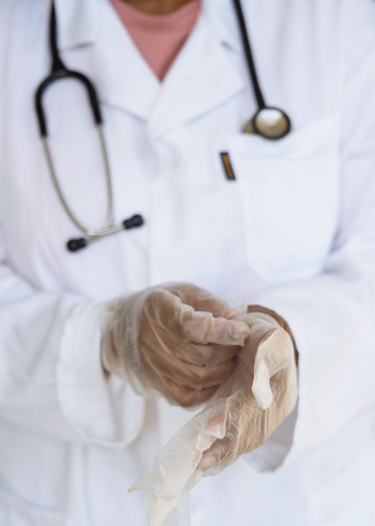A doctor in a white coat putting on gloves.