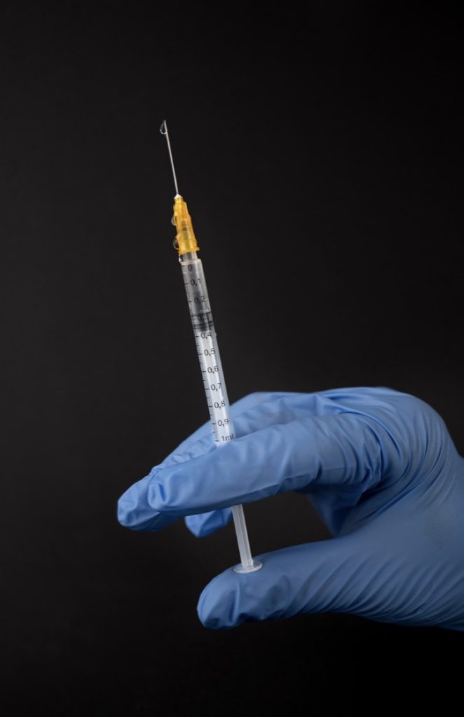 syringe held by hand in blue glove on black background