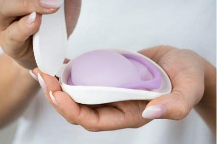 A purple diaphragm in a white case. A person's hands are shown holding the case open.