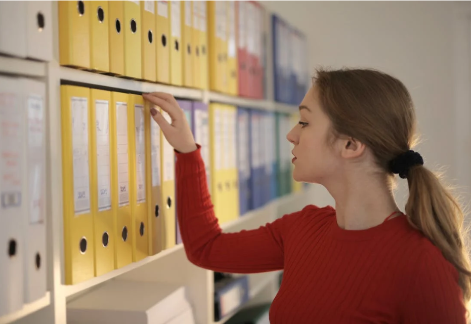A person going through a shelf of organized binders filed by color.