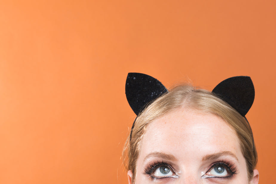 A person is wearing cat ears and eyeliner in front of an orange background. 