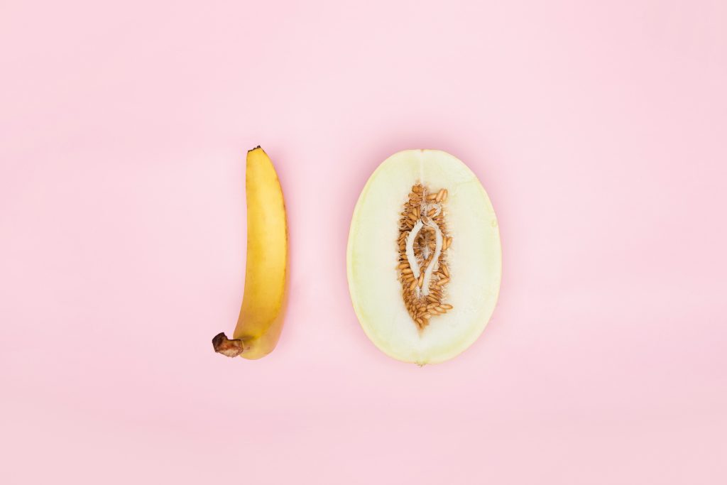 A banana and a melon cut in-half against a pink background.