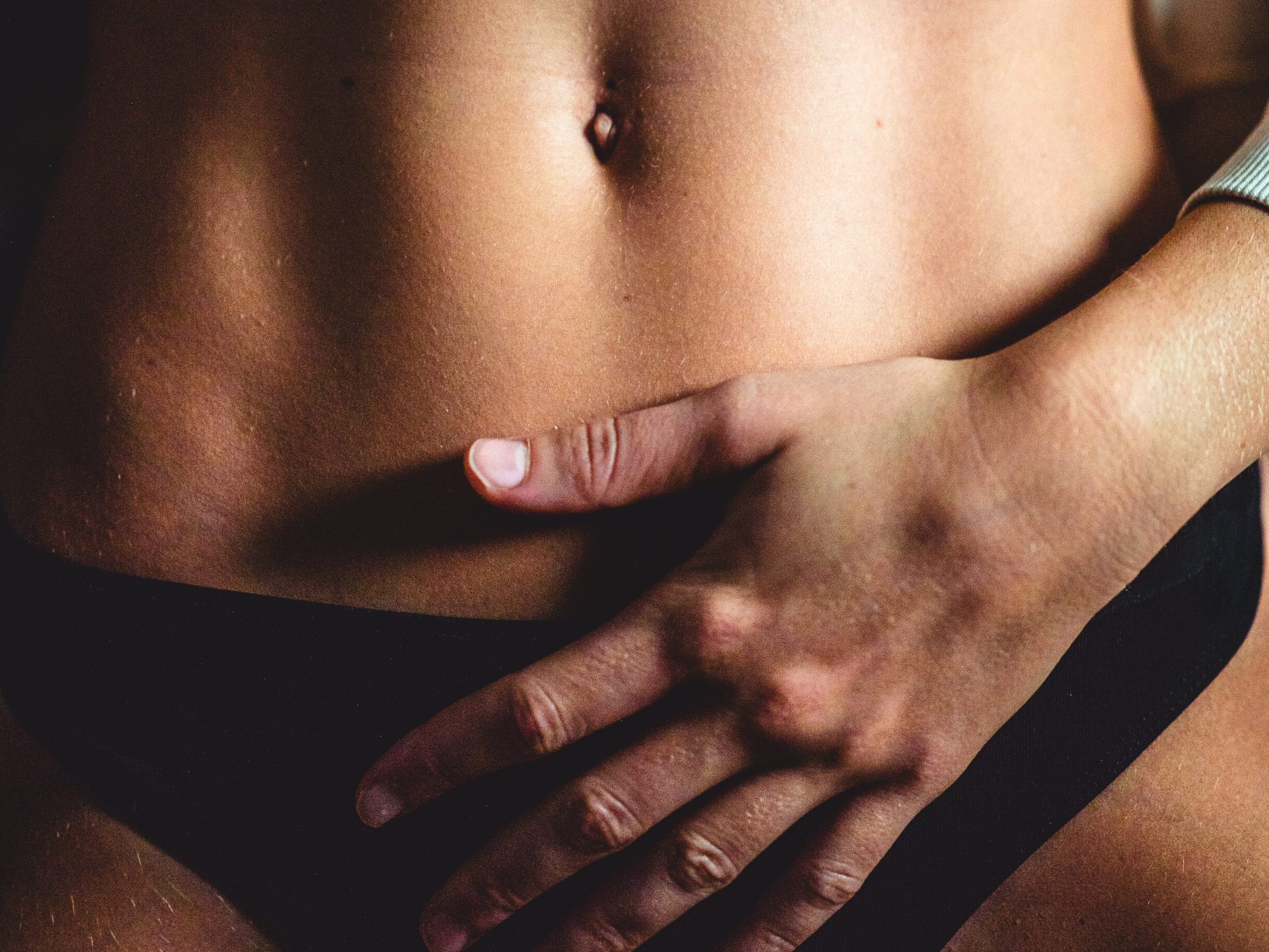 Close-up of a person's abdomen with their hand over it, appearing to be rubbing it.