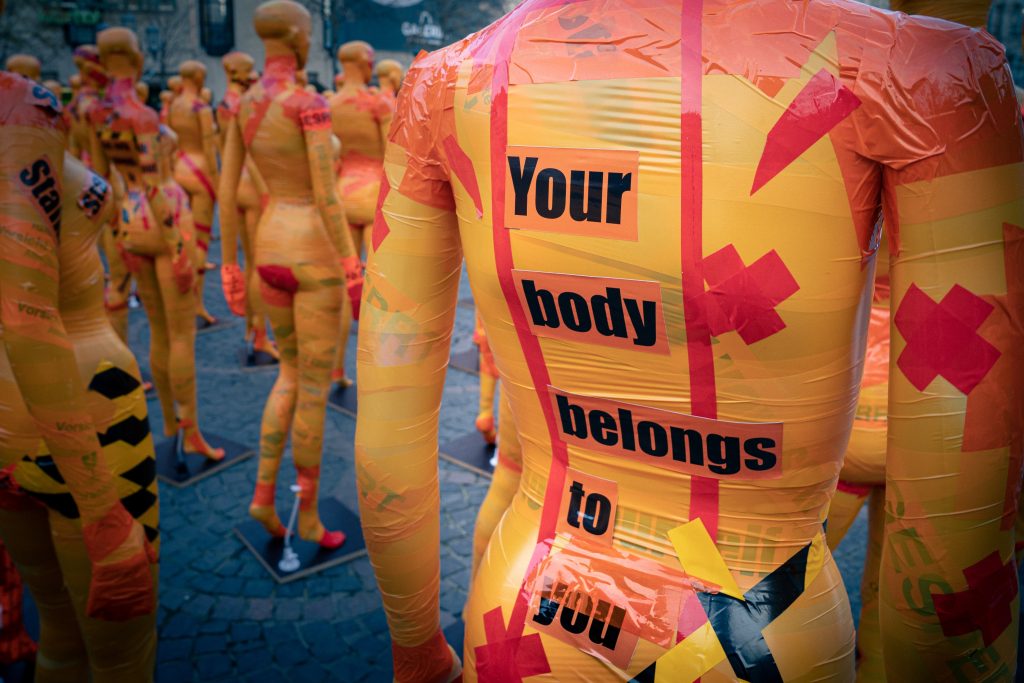 Multiple mannequins wrapped in orange and red tape. One of the mannequin's back has "your body belongs to you" written on it.