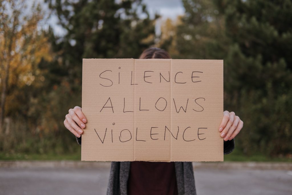 A person is holding a cardboard sign that says "Silence Allows Violence."
