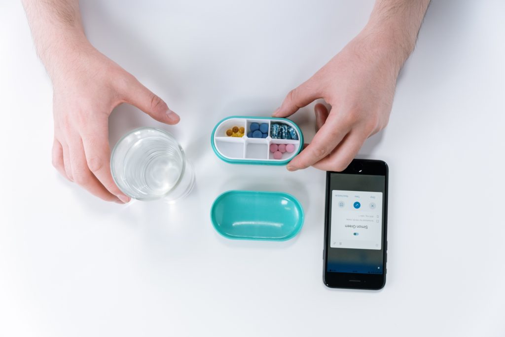 An oval box filled with pills and a glass of water next to it. There is a phone beside the pills.