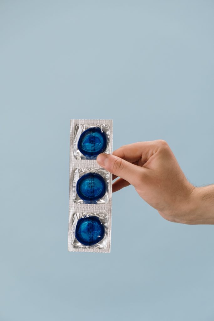 A hand holding three blue condoms.