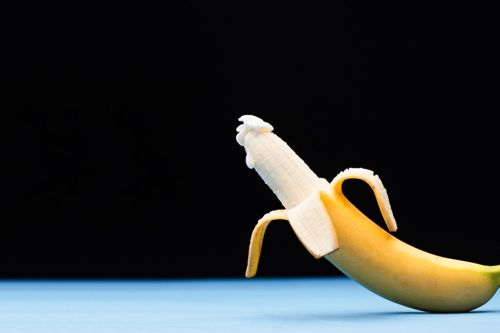 A banana half-way peeled and with a milky substance on the tip.