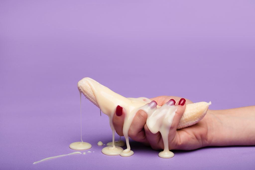 A hand holding a banana with a creamy substance dripping.