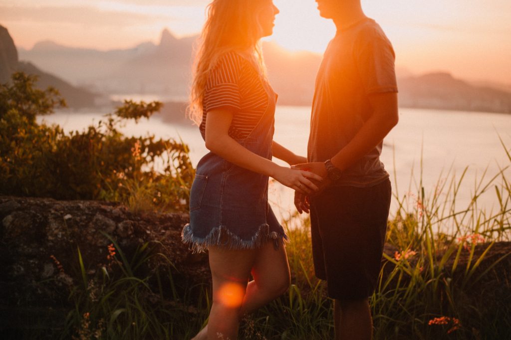 A couple holding hands outdoors. There is a sunset.