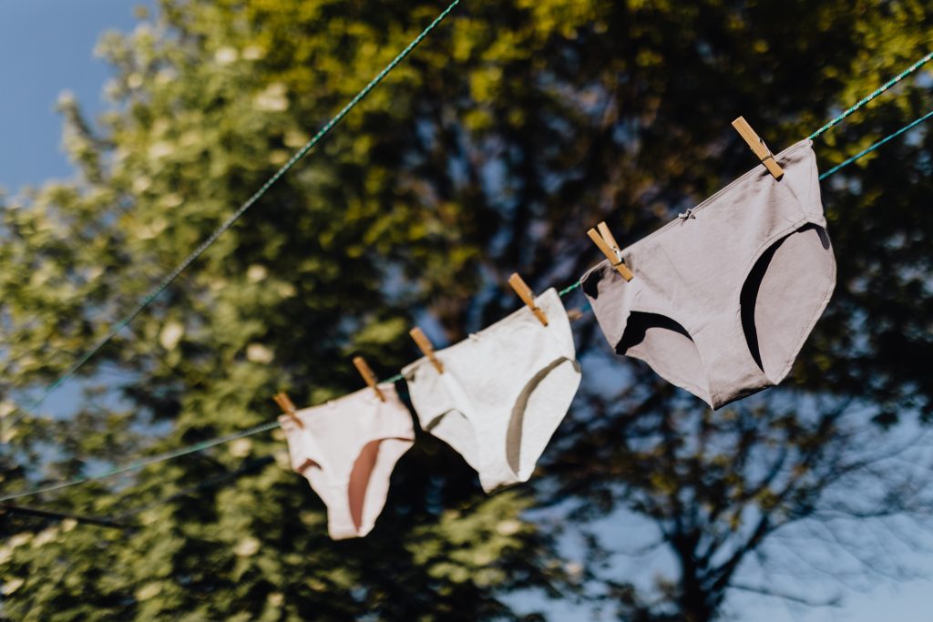 Three pairs of underwear hung on a clothesline hanger outdoors.