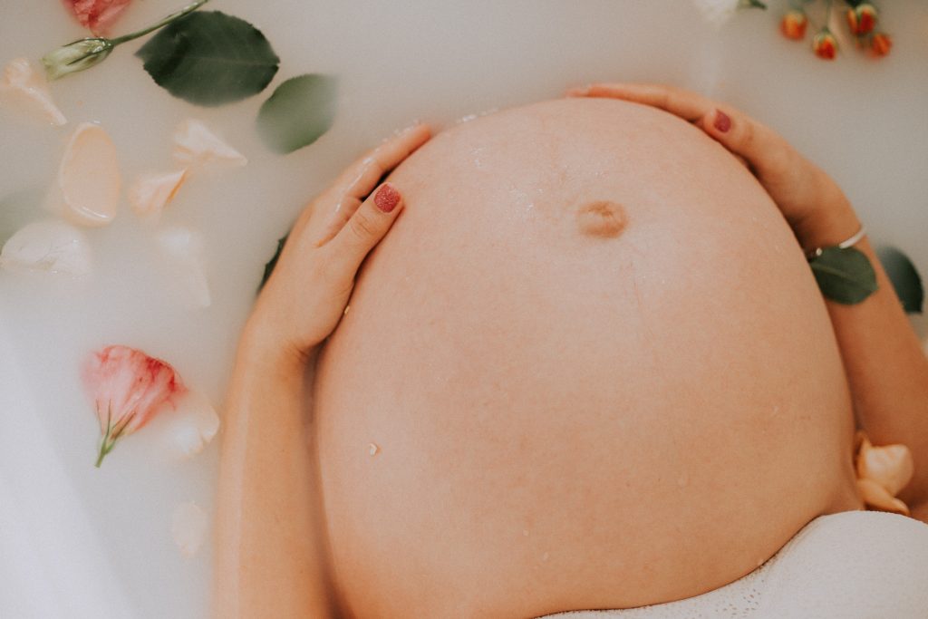 A pregnant belly in a milky bath with flower petals.