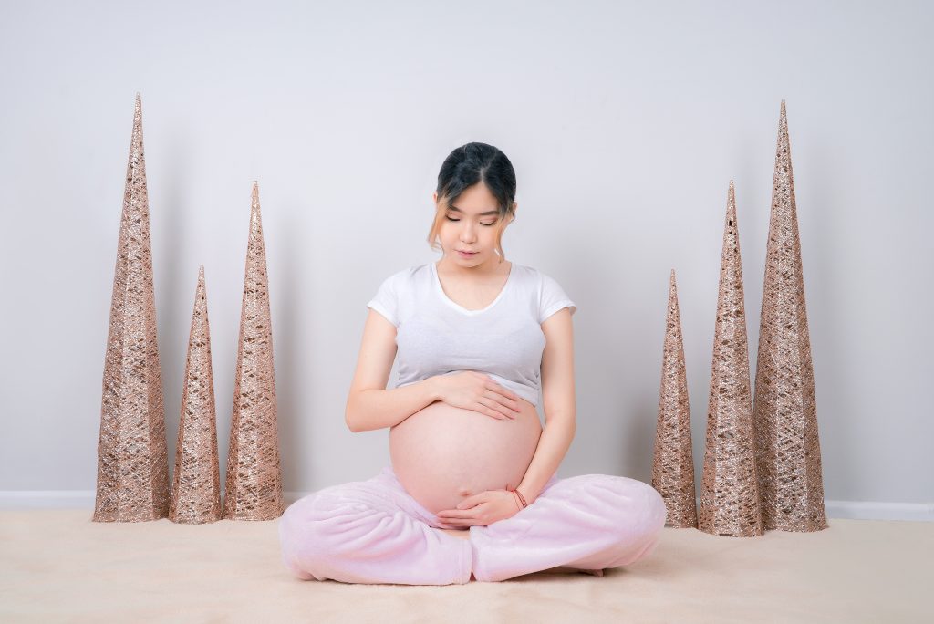 A pregnant person sitting on the floor while holding their belly. There are pink glitter cones beside the person.