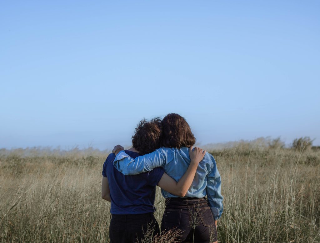 Two individuals hugging while standing in a field of tall grass.