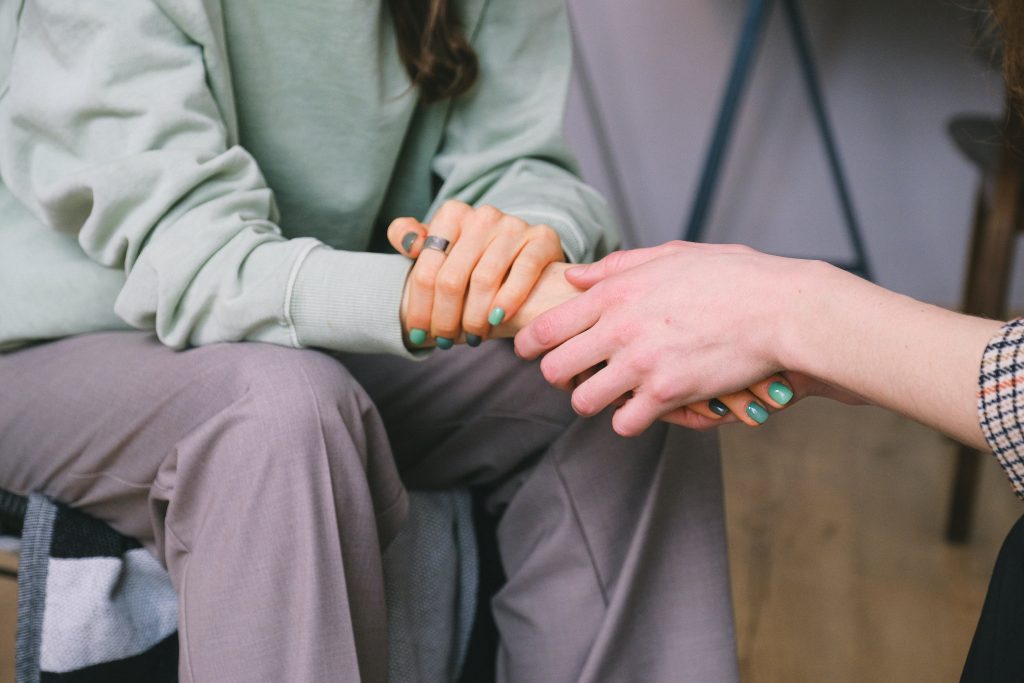 An individual's hand holding on to another person's hand while they are sitting.