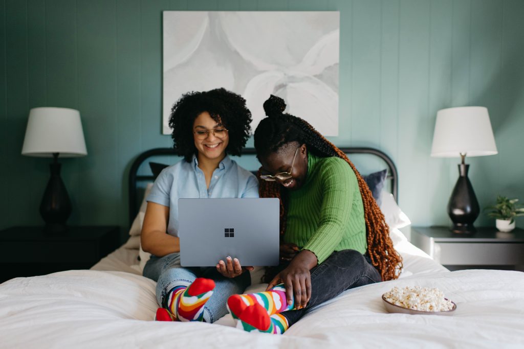 A couple laughing together over what is on their laptop while sitting on their shared bed