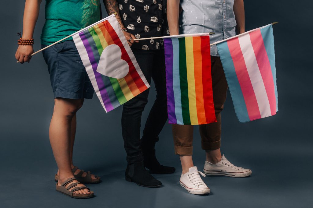 Three people standing together holding pride flags. 