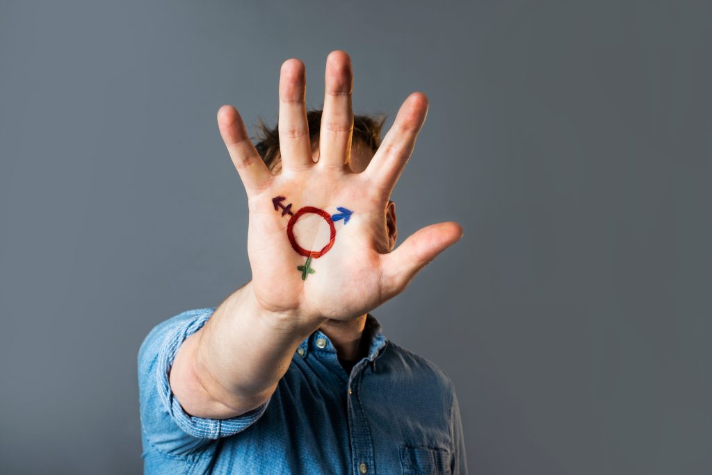 Palm of a hand with the transgender symbol on it.  The symbol is a circle with an arrow, a cross, and an arrow with a cross pointing out from it. 